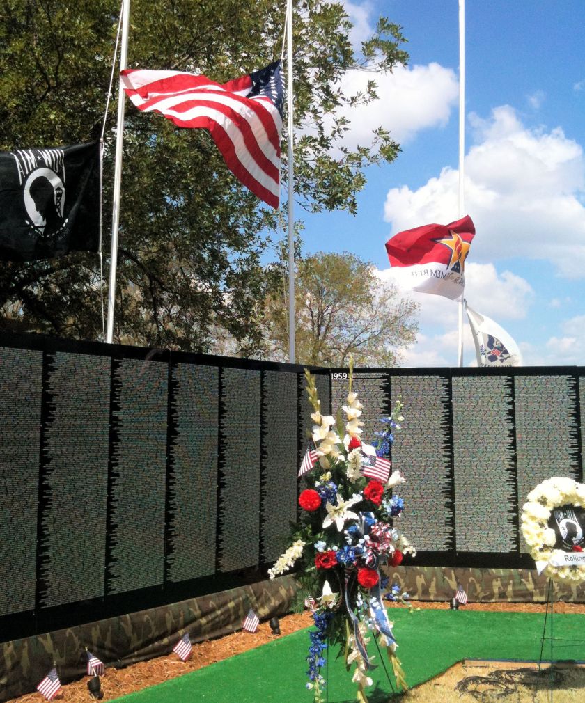 a replica of the Vietnam Memorial Wall with an American flag and a wreath of red, white, and blue flowers