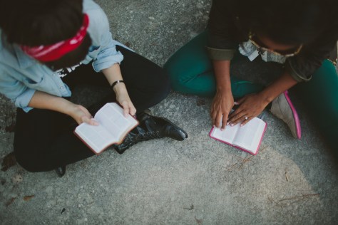 two women sitting on a rug with open books