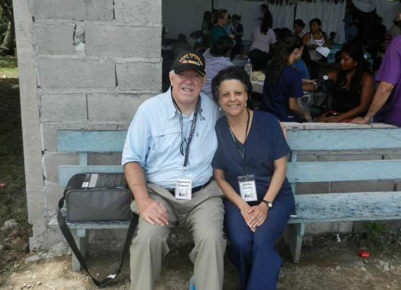 a woman in a medical scrub suit and man with army veteran cap, in a rural setting