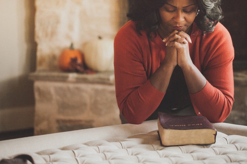 a women with hands clasped in prayer with a Bible