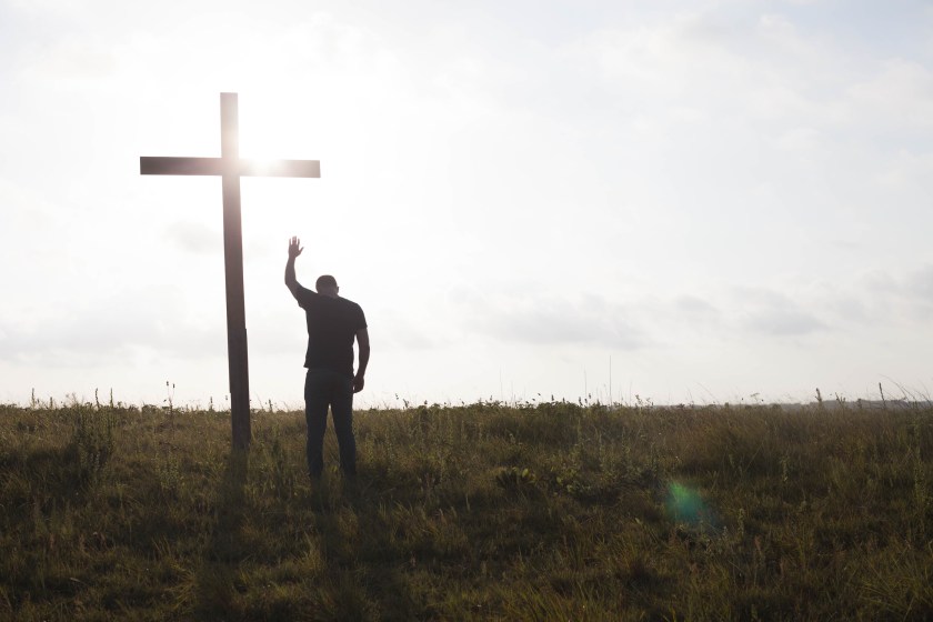 man standing in front of a cross with one arm raised