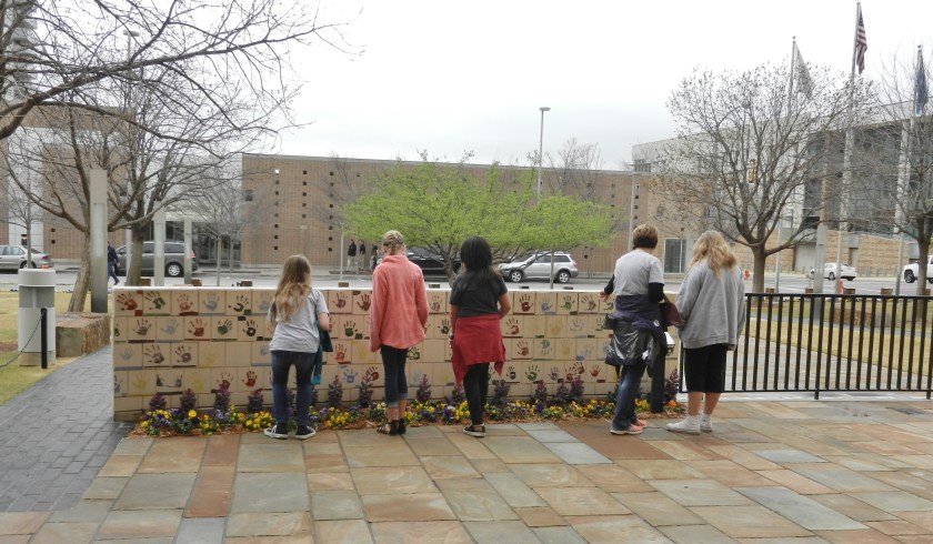children and adults visiting a wall decorated with handprints