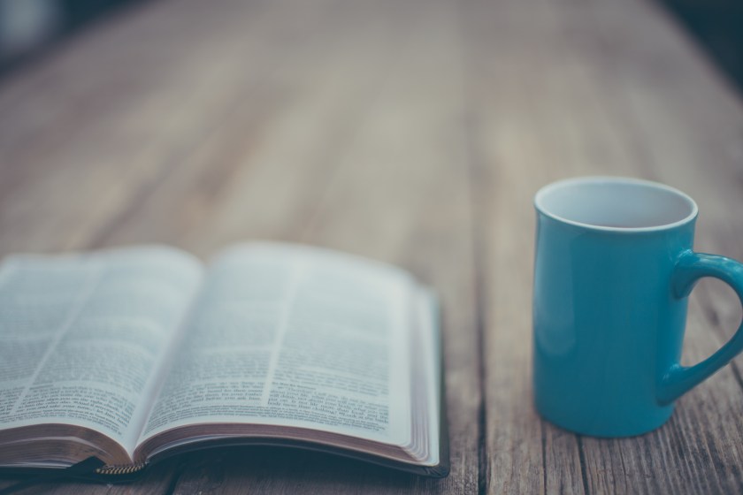an open Bible lying on a table, next to a mug