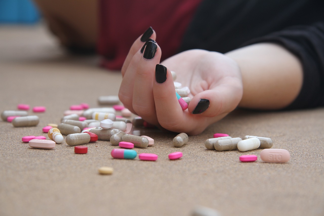 woman with palm full of pills and pills scattered on the floor