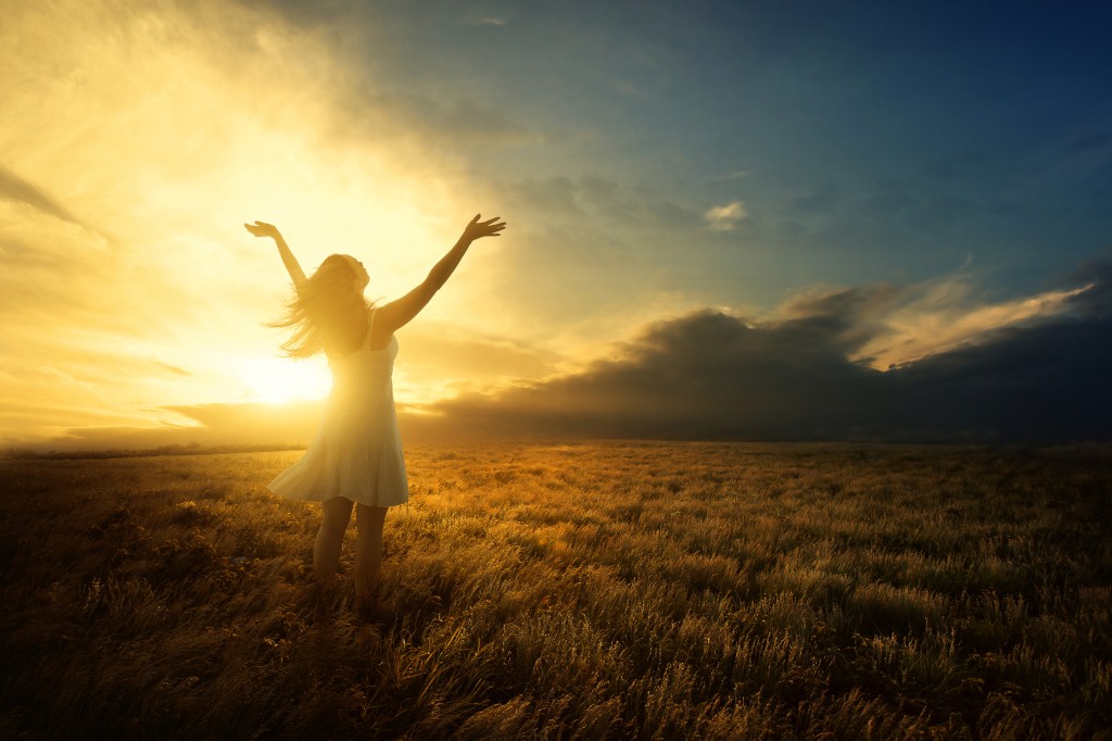 woman raising arms arms to the sky in a glow of light