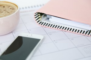 a smartphone lying on a calendar page with a planner and cup of coffee