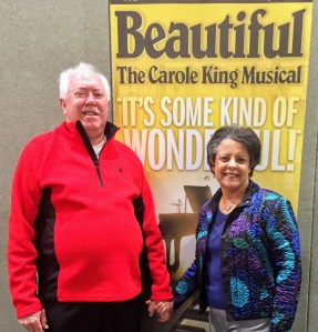 husband-wife couple holding hands in front of poster for Beautiful The Carole King Musical
