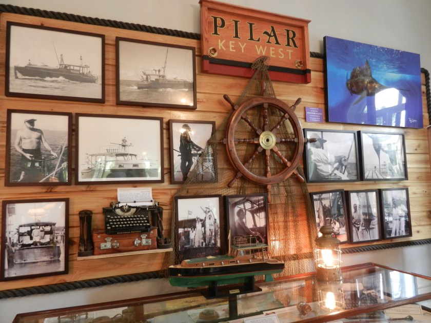 old photographs , a boat model, and a steering wheel, hanging on a wall at the Hemingway Home Museum