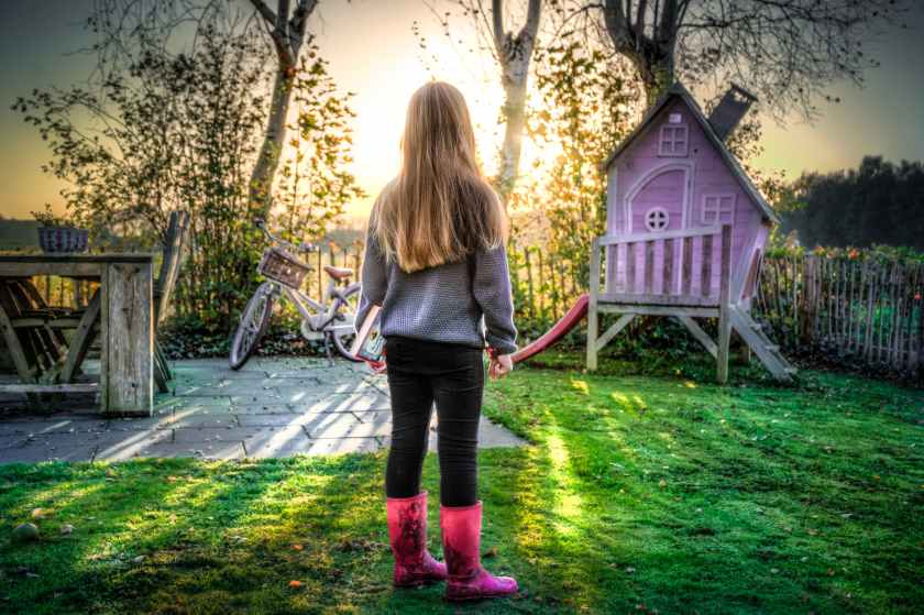 young girl in bright pink boots next to a pink playhouse in her yard
