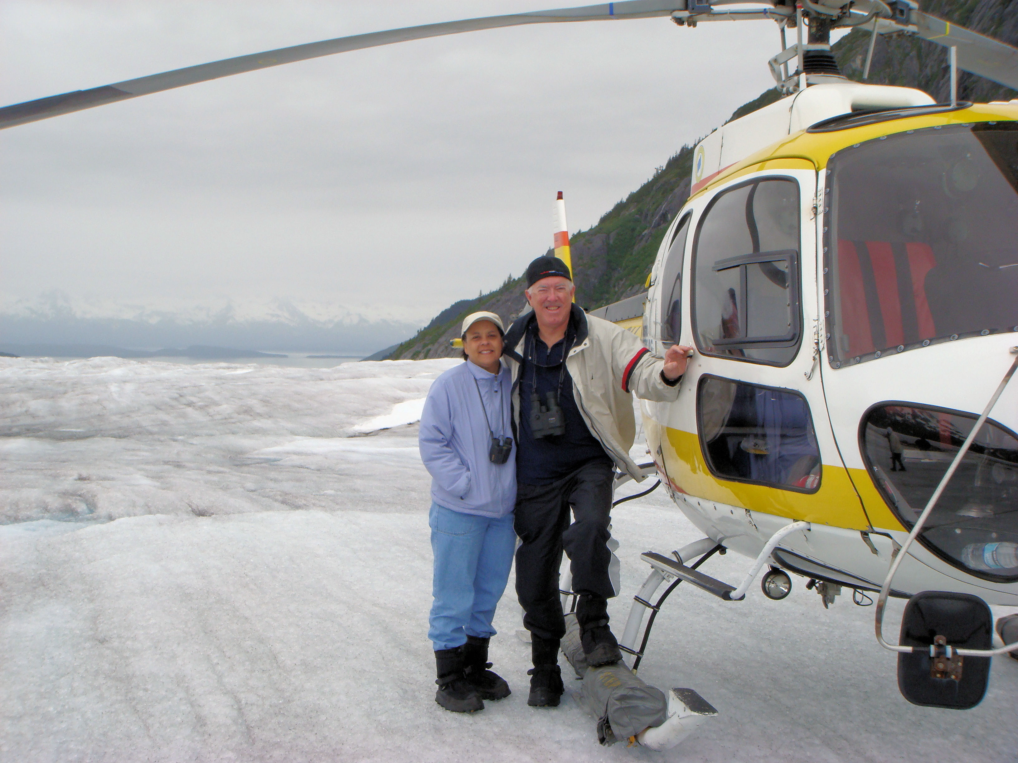 man and woman standing next to a helicopter on a glacier