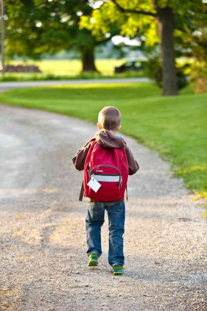 little boy walking down a dirt road with a red backpack