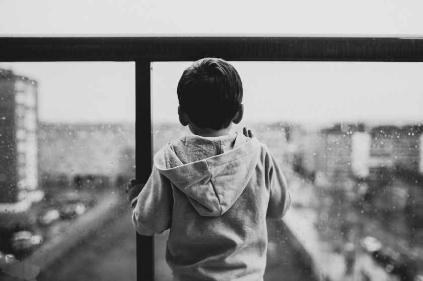 little boy in a hoody, looking out a rainy window