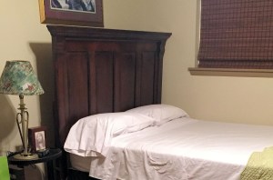 a simple bed, window shade down, small lamp on a side table