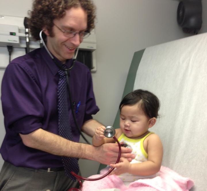 a male doctor examining a smiling baby girl