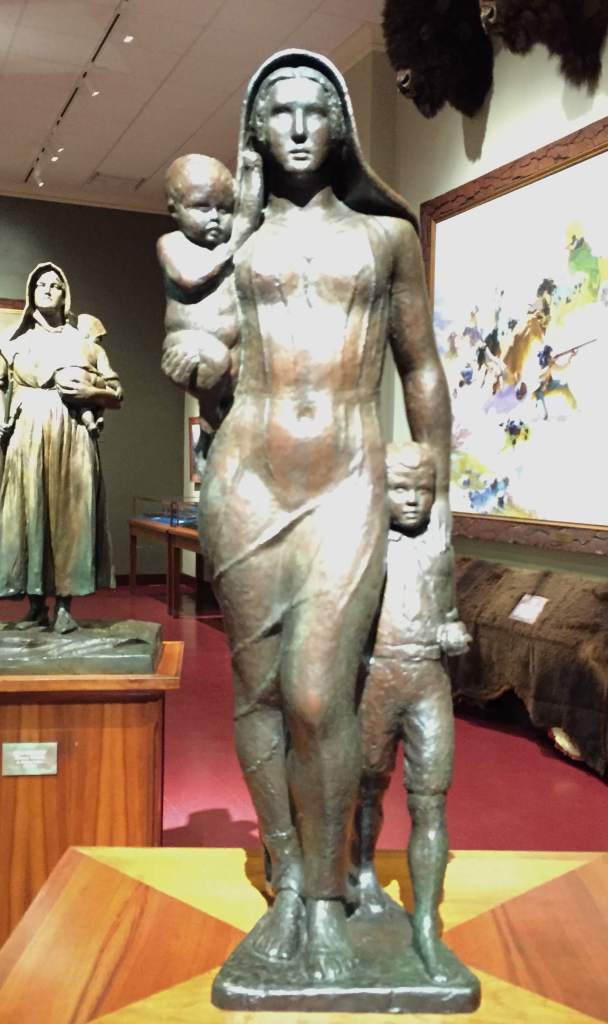 statue of woman, holding infant, standing next to a child