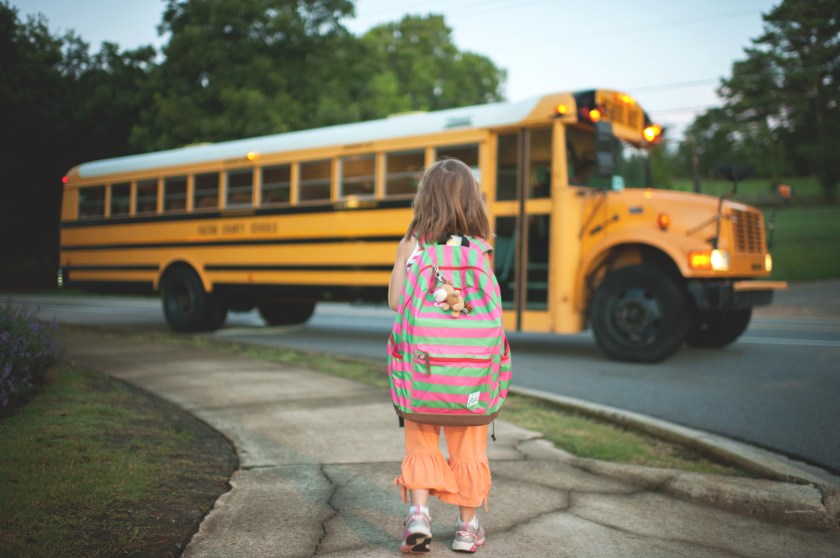a girl with a large backpack, walking to a school bus