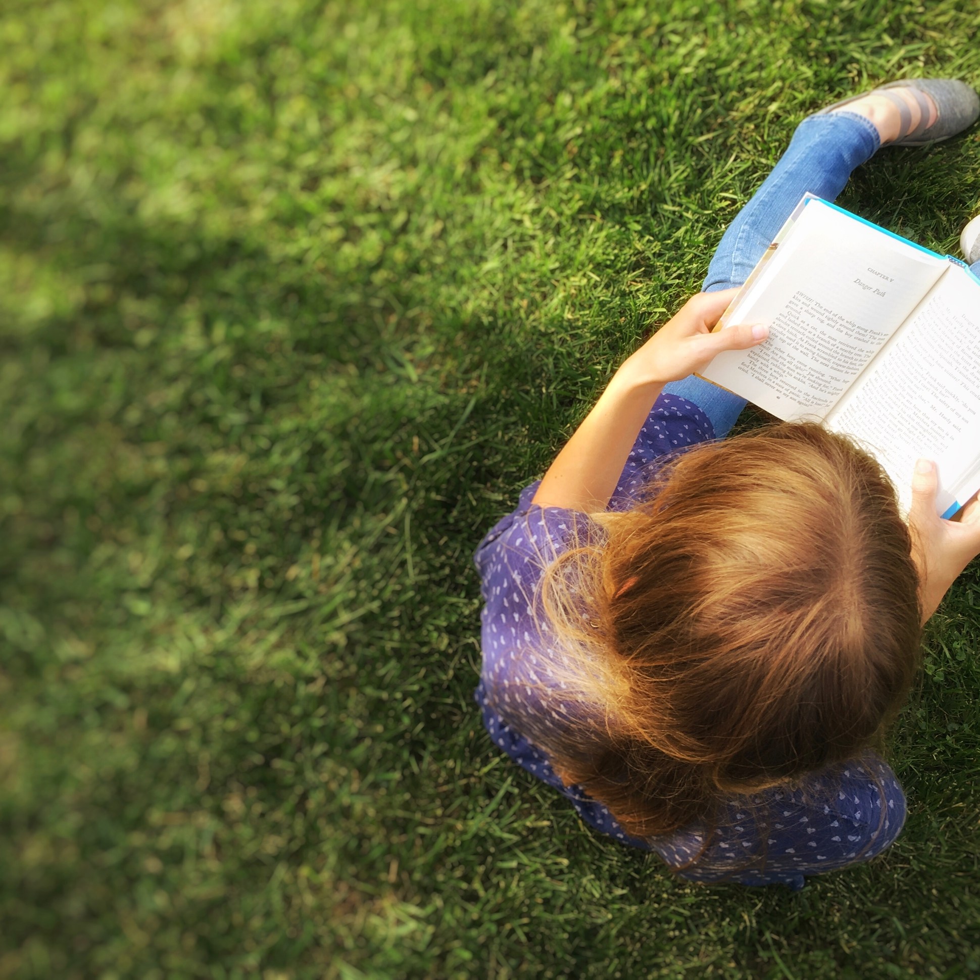 a girl sitting in grass reading a book.