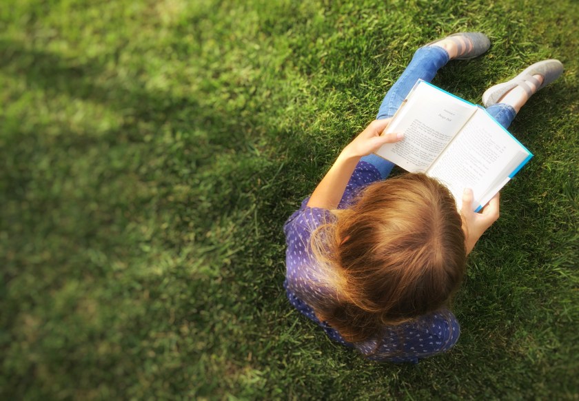 a girl sitting in grass reading a book.