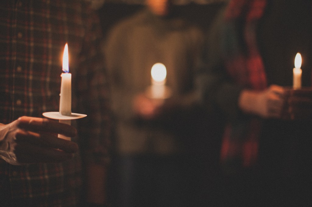 three people, blurred, holding lit candles