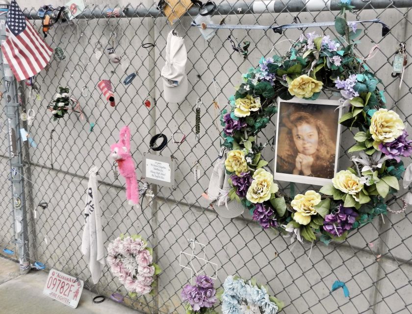a chainlink fence with mementos-wreath, photo, flag, ball cap