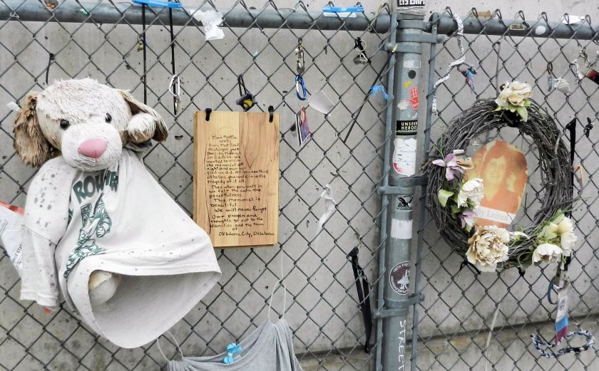 a chainlink fence with mementos-stuffed dog, wreath, photo, plaque
