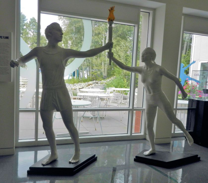 white statues of 2 runners handing off the Olympic torch