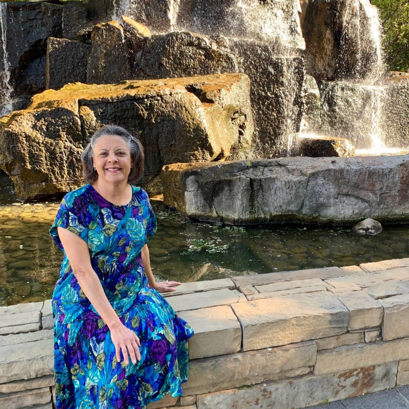 Dr Aletha in a print dress sitting by a waterfall
