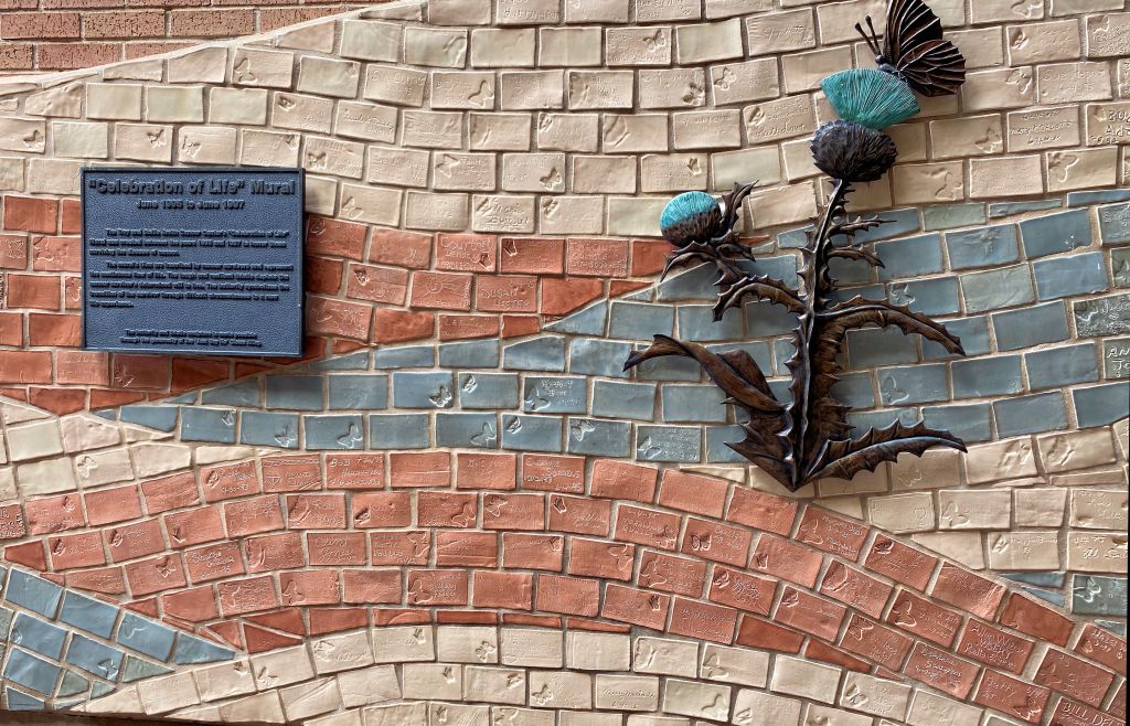 a wall decorated with inscribed bricks and a metal floral sculpture