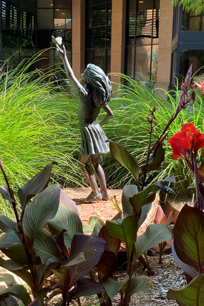 GIRL STATUE, BUSHES, RED FLOWER