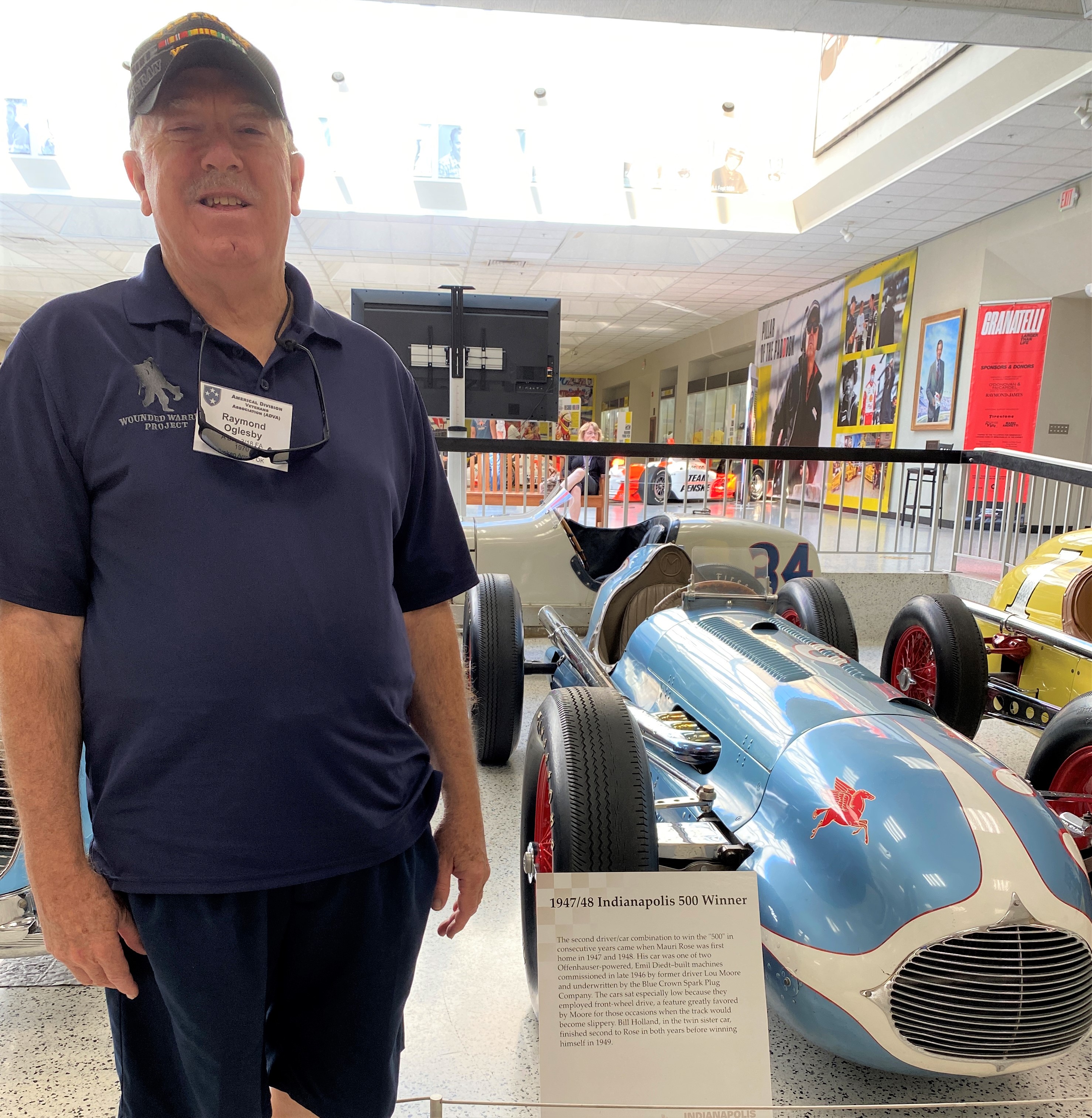 a man standing by a blue race car at Indy race museum