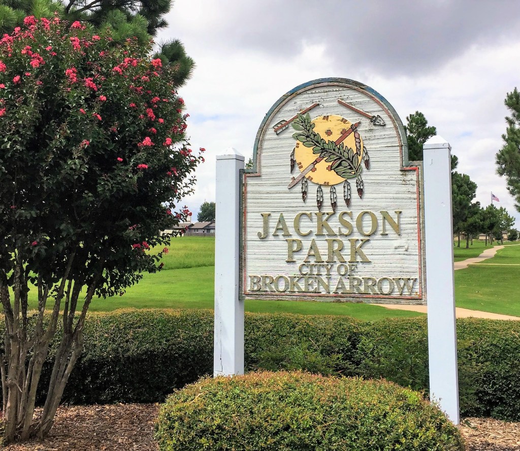a sign-JACKSON PARK CITY OF BROKEN ARROWsurrounded by shrubs