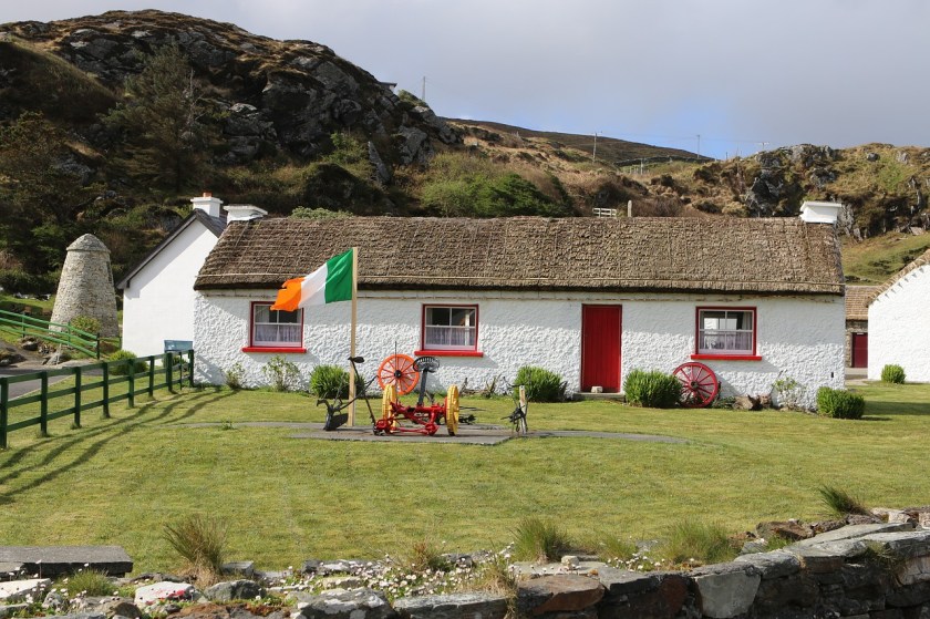 a lovely white cottage with a red door, with an Irish flag in the yard