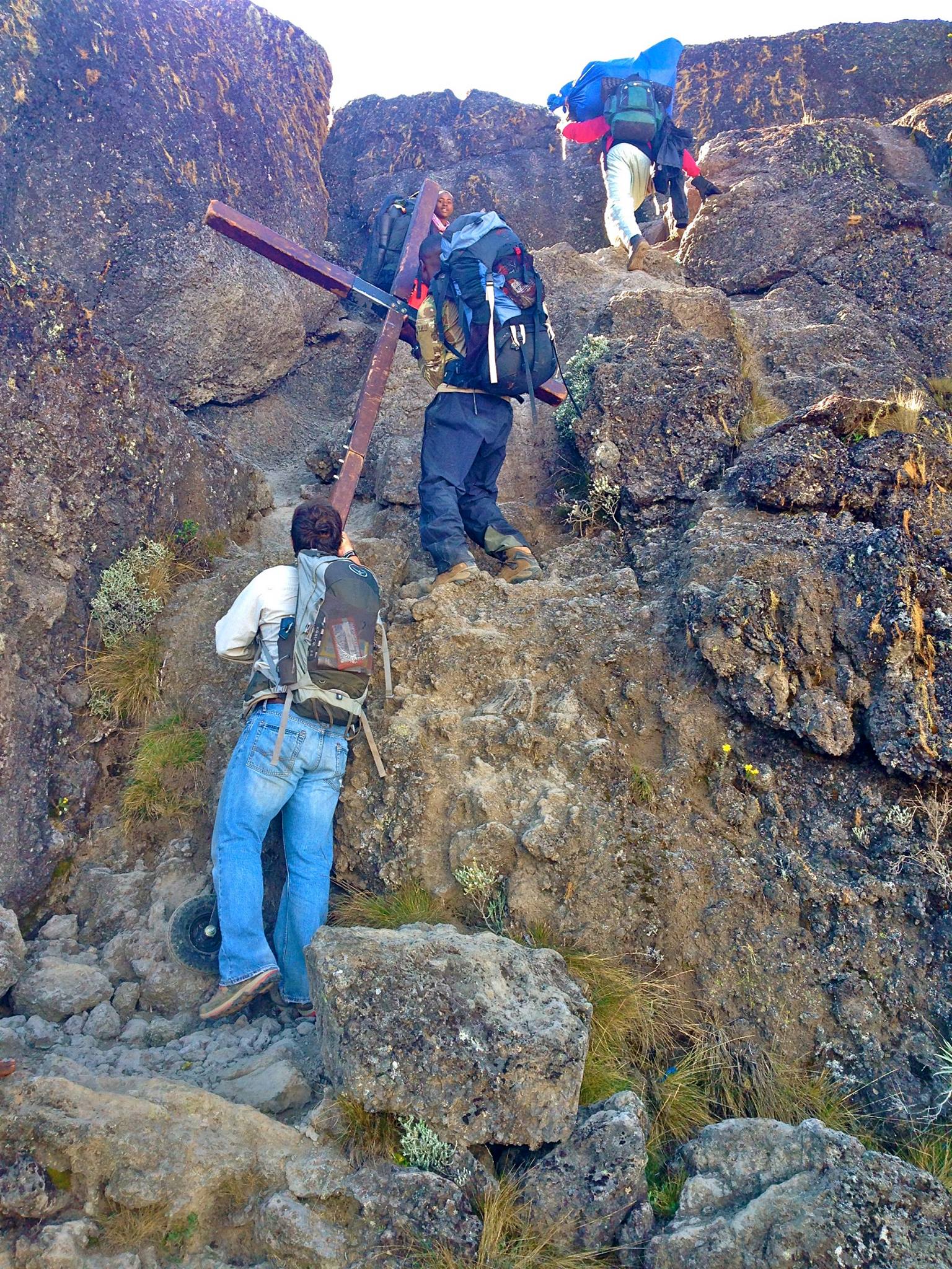 men carrying a cross up a rugged mountain wall