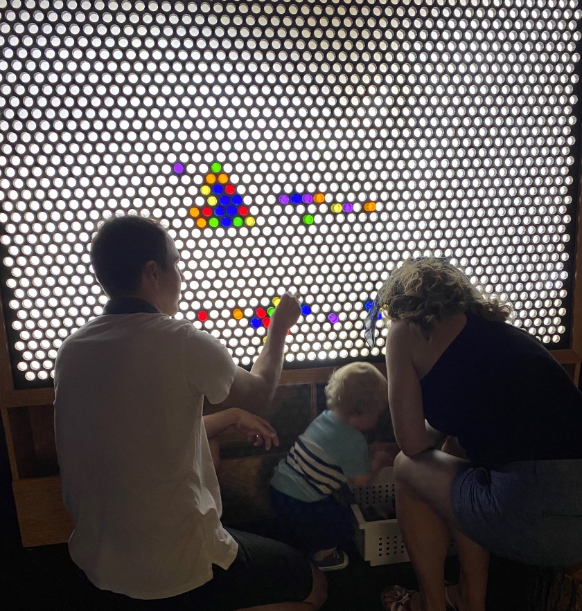 parents and child playing with a interactive board of colored round balls
