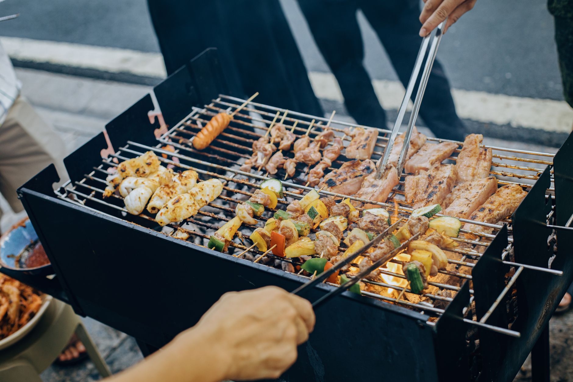 A grilling barbecue with various skewered meats and vegetables, including chicken, sausages, and bell peppers, being cooked over an open flame.